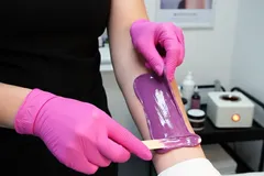 Depilace voskem na ruce, profesionální kosmetička v růžových rukavicích nanáší vosk.